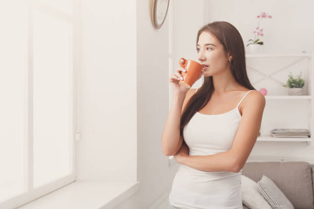 istock Pensive woman standing near window with coffee 866068316