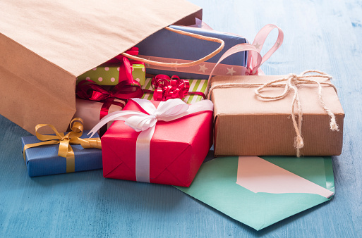 Colorful gift boxes coming out on a blue wooden table from a paper shopping bag