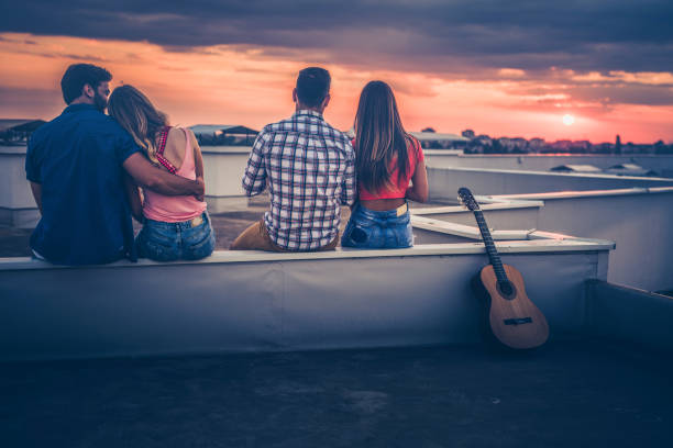 istock Back view of two couples sitting on rooftop at sunset. 866072346