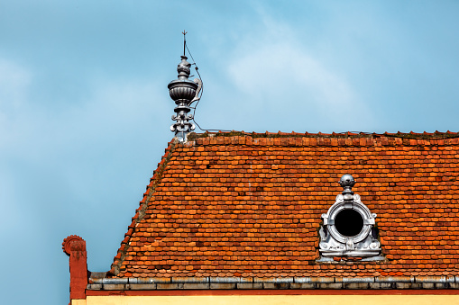 Shingle roof of old house with decoration on gableand a round window against blue sky