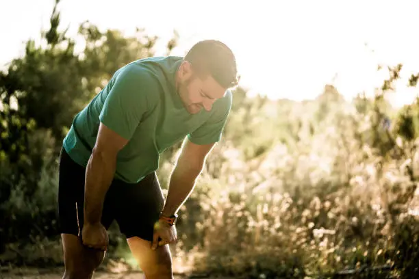 Photo of Tired male runner bending in forest