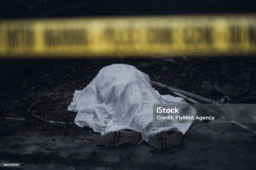 Dead body on the ground behind a cordon tape The dead body is seen lying on the ground behind a cordon tape. Dead Person Stock Photo