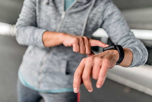 Closeup of smart watch on female hand. Girl dressed in gray sweatshirt  and using digital gadget. Young woman presses a finger on the side button smartwatch.Student using smart watch checking messages.  Maure Female running in the city during autumn day. Senior sportswoman using smartwatch to track her workout performance. Fitness female monitoring her progress.