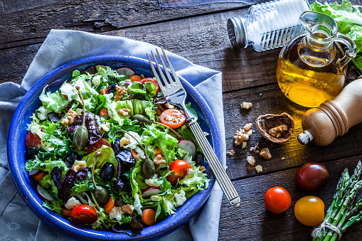 High angle view of a fresh organic salad served in a blue plate shot on rustic wooden table. The plate is at the left side of an horizontal frame on a bluish textile napkin and a salt and pepper shakers as well as an olive oil bottle are at the right placed directly on the wooden table. Predominant colors are green and blue. DSRL studio photo taken with Canon EOS 5D Mk II and Canon EF 100mm f/2.8L Macro IS USM