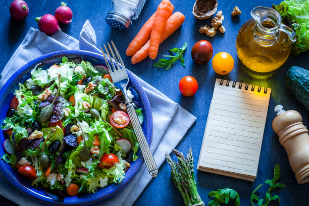 istock Fresh salad plate with cookbook on bluish kitchen table 866154380