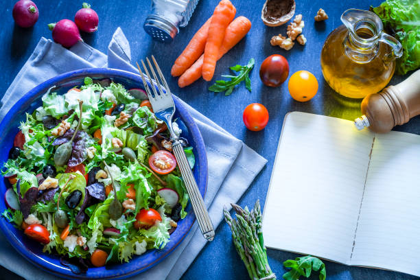 istock Fresh salad plate with cookbook on bluish kitchen table 866155044