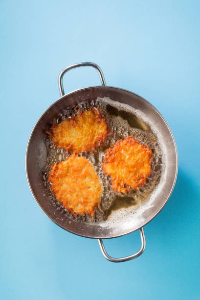 frittelle di patate latkes sono cotti in olio su una padella di metallo su sfondo blu - latke foto e immagini stock