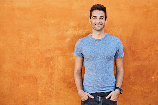 Guy in blue t-shirt against orange wall, smiling