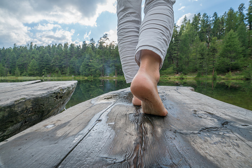 View of lower woman's body part standing on wooden lake pier