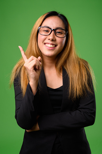 Studio shot of young Asian businesswoman with dyed hair against green background