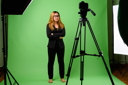 Studio shot of young Asian businesswoman vlogging against green background