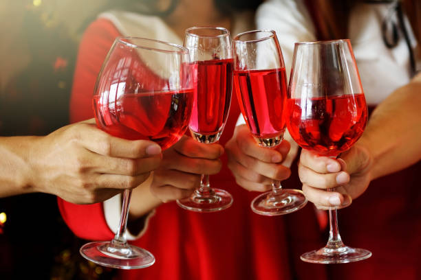 Group of young hands with red wine toasting glasses for Christmas or xmas celebrating party. Closeup photo with bokeh background for ceremony holiday