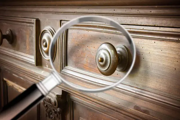 Photo of Detail of an antique wooden italian furniture just restored with a magnifying glass on foreground looking for woodworm threat detection