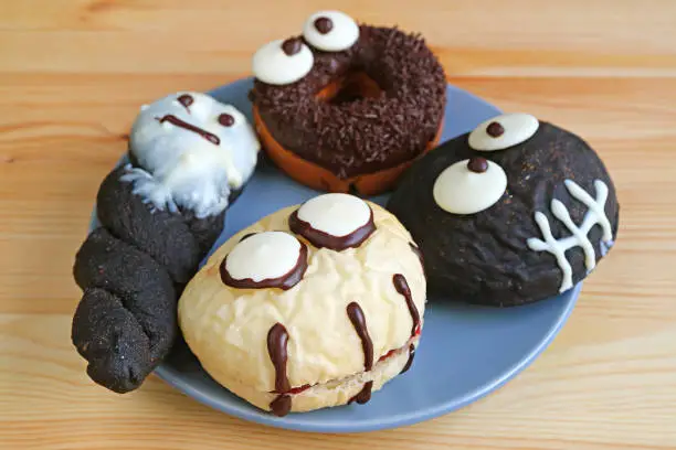 Plate of Assorted Halloween Monsters and Ghosts Shaped Doughnuts Served on Wooden Table