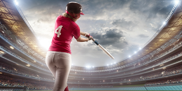 Softball female player on a professional arena. Beautiful athlete with sport bat in unbranded uniform on big arena. The player beats the ball.