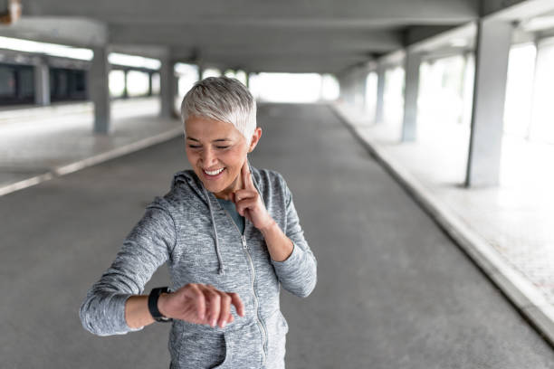 Watching her heart rate Mature, gray hair woman checking results after jog in the park. Attractive looking mature, short hair female keeping fit and healthy. Joyful senior lady using tracker after exercising. Runner checking pulse after exercising with her smart watch. Smiling runner checking heart rate after exercising. Concept sport and fitness cardiac conduction system stock pictures, royalty-free photos & images