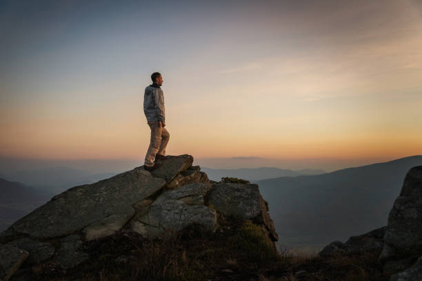 istock Man standing on rock on mountain top at sunset 866236376