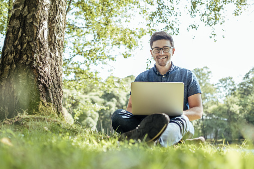 Young man with laptop outdoor sitting on the grass. Remote working concept