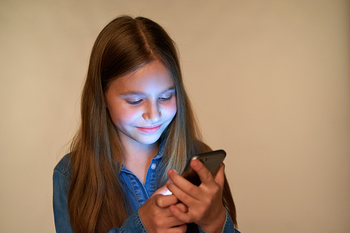 Closeup smiling little girl using smart phone with glowing screen