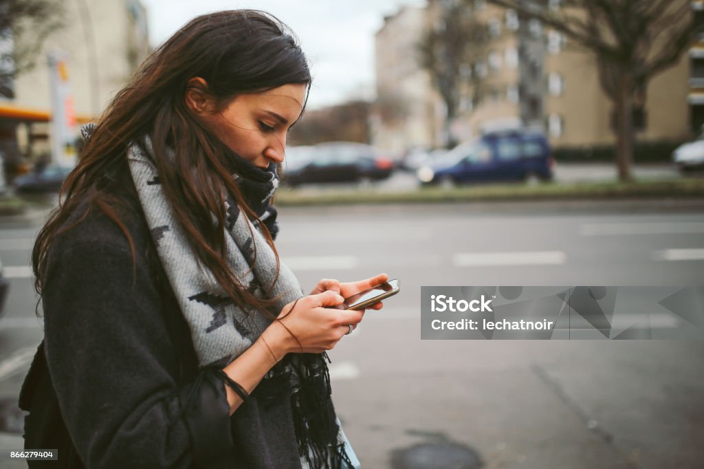 Young woman walking in Berlin, checking her mobile phone Vintage toned portrait of a young woman walking in Berlin, in the Schoneberg district of West Berlin, wearing casual clothing, a gray coat and a scarf, checking her mobile phone. Winter Stock Photo