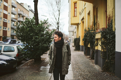 Vintage toned portrait of a young man walking in Berlin, in the Schoneberg district of West Berlin, wearing casual clothing, an olive green classic military parka and a scarf.