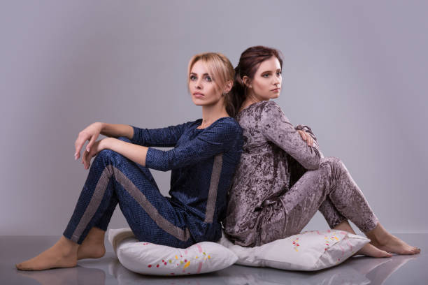 istock Two women in pajamas sit on pillows on a gray background. 866291232