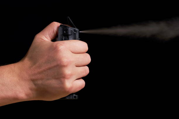 self defense - using pepper spray man aiming and spraying pepper spray with visible fog on black background mace spice stock pictures, royalty-free photos & images