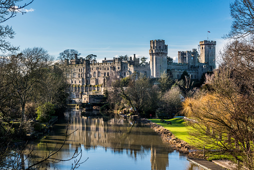 Warwick, England, United Kingdom - Feburary 04, 2017: The photo shows Warwick Castle in Warwickshire in England, UK on a sunny day with blue sky. The  national landmark is visable in the background. Avon river and reflections are visable in the foreground.