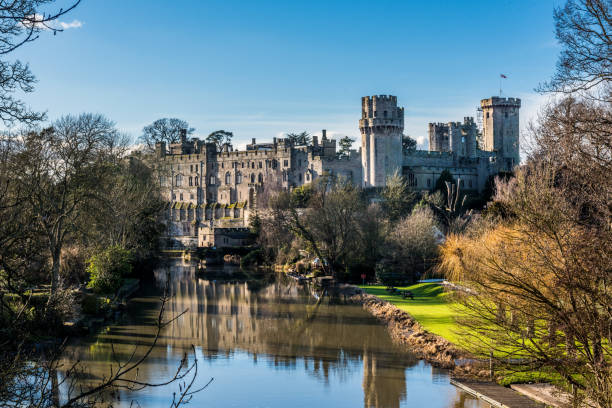 Warwick castle photographed on a sunny day in springtime with blue sky and copy space Warwick, England, United Kingdom - Feburary 04, 2017: The photo shows Warwick Castle in Warwickshire in England, UK on a sunny day with blue sky. The  national landmark is visable in the background. Avon river and reflections are visable in the foreground. warwick uk stock pictures, royalty-free photos & images