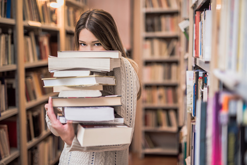 Beautiful teenage girl hiding behind a stack of books