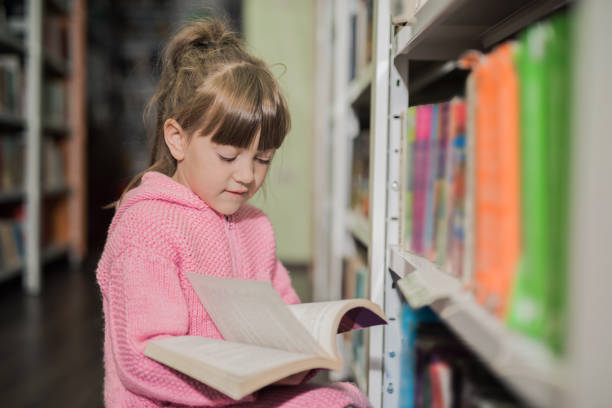 istock Young girl reading a book in a library 866337048