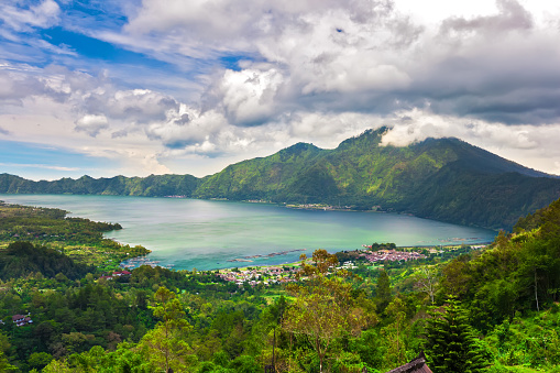 Panoramic view of a lake surrounded by mountain, tropical landscape with colorful clouds in the sky. Fisheries and settlements on the shore.