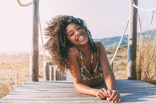 Beautiful young black woman lying down in a  wooden foot bridge at the beach