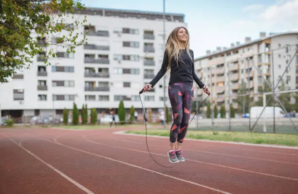 28 years old woman is exercising outdoors. She is jumping rope, which is always her last exercise