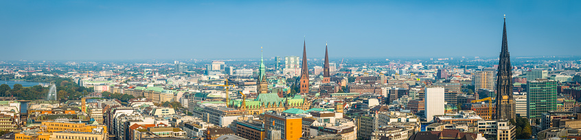 Aerial panorama over the spires and rooftops of central Hamburg, from the iconic tower of the Rathaus to the blue waters of Binnen Alster lake, Germany.