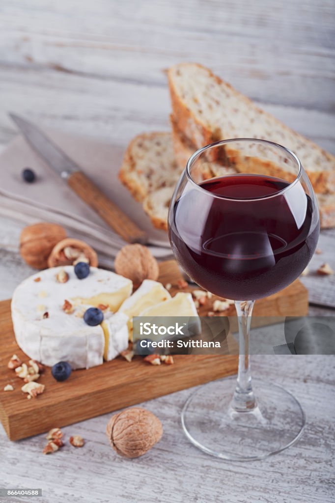 Soft french cheese of camembert. Soft french cheese of camembert served with chopped walnuts, glass of red wine and blueberries on wooden plate. Alcohol - Drink Stock Photo