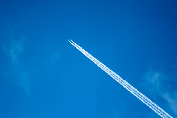 jet airplaneaircraft with condensation trails on blue sky flying across a pure blue sky diagonally, leaving behind a long white stream of con trail. - con trail imagens e fotografias de stock