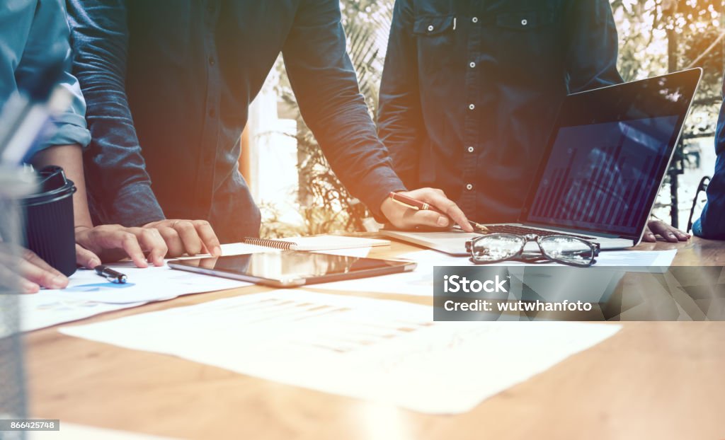 Three businessmen working on laptop computer with documents and paperwork scattered around and digital tablet on desk. Advice Stock Photo