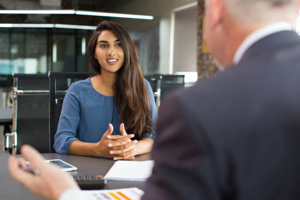 Smiling female client talking to male manager Portrait of young Indian female client or candidate sitting at table, talking to senior male manager and smiling in office. Job interview or consultancy concept job interview stock pictures, royalty-free photos & images