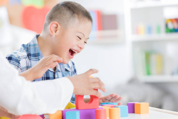 Unrecognizable teacher helps young boy with blocks Cheerful preschool age boy enjoys playing with blocks with his teacher. Only the teachers arms are seen in the photo. special education stock pictures, royalty-free photos & images