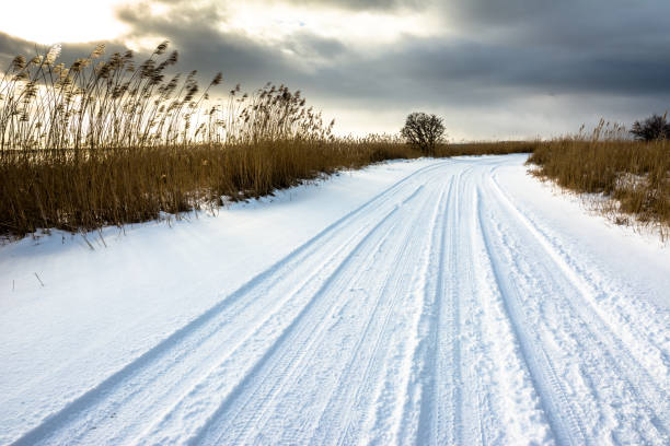neige sur la route, paysage d’hiver avec mauvaise humeur ciel avant de coucher de soleil sur le lac - frozen cold lake reed photos et images de collection