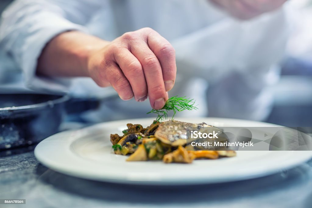 Chef in cucina in hotel o ristorante cucina, solo mani. Bistecca di pesce preparata con decorazione aneto - Foto stock royalty-free di Cuoco
