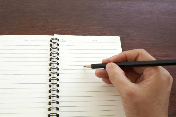 istock Woman hand with black pencil writing on blank notebook on wooden table. 866478588