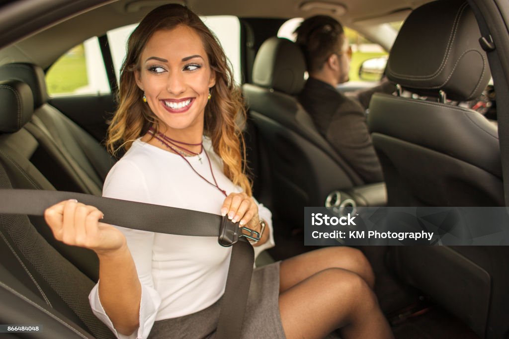 Beautiful businesswoman putting on seatbelt in car Beautiful businesswoman putting on seatbelt in car with chauffeur in background Chauffeur Stock Photo