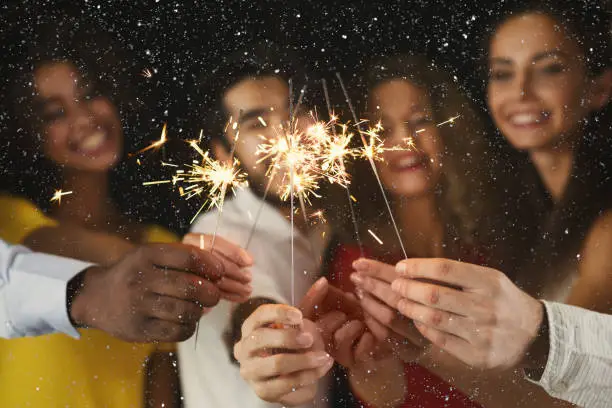 Holiday background with sparklers. Young friends holding bengal lights, closeup, selective focus. Birthday or winter holidays celebration, greeting card mockup