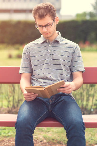 istock Young man reading a book in park 866498210