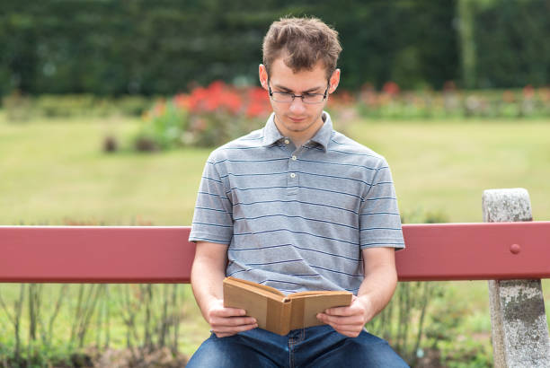 istock Young man reading a book in park 866498218