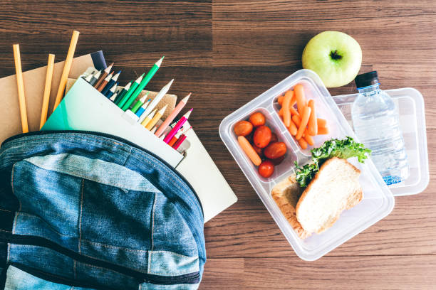 Lunch box with vegetables and slice of bread for a healthy school lunch on wooden table stock photo