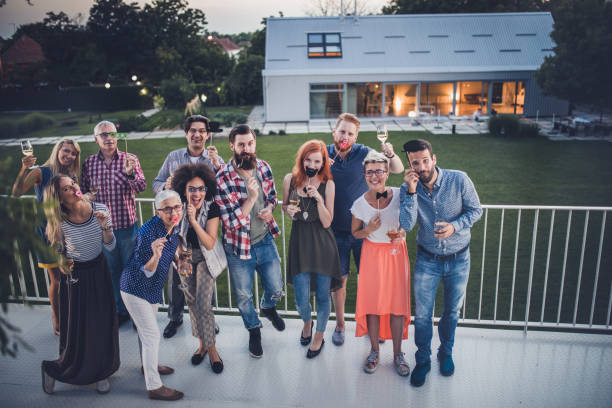 Large group of playful business colleagues having fun on a terrace party. Crowd of happy freelancers having fun during a party on a terrace and looking at camera. women movember mustache facial hair stock pictures, royalty-free photos & images