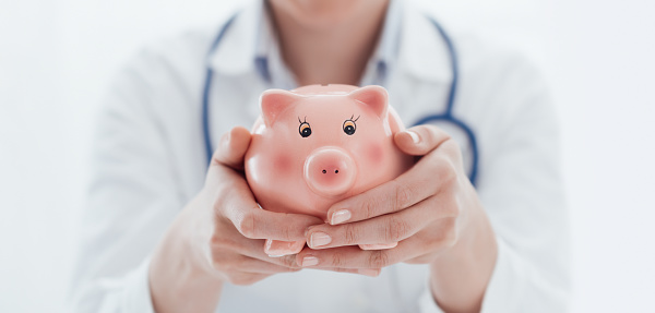 Female doctor holding a piggy bank: health insurance, medical expenses and tax concept